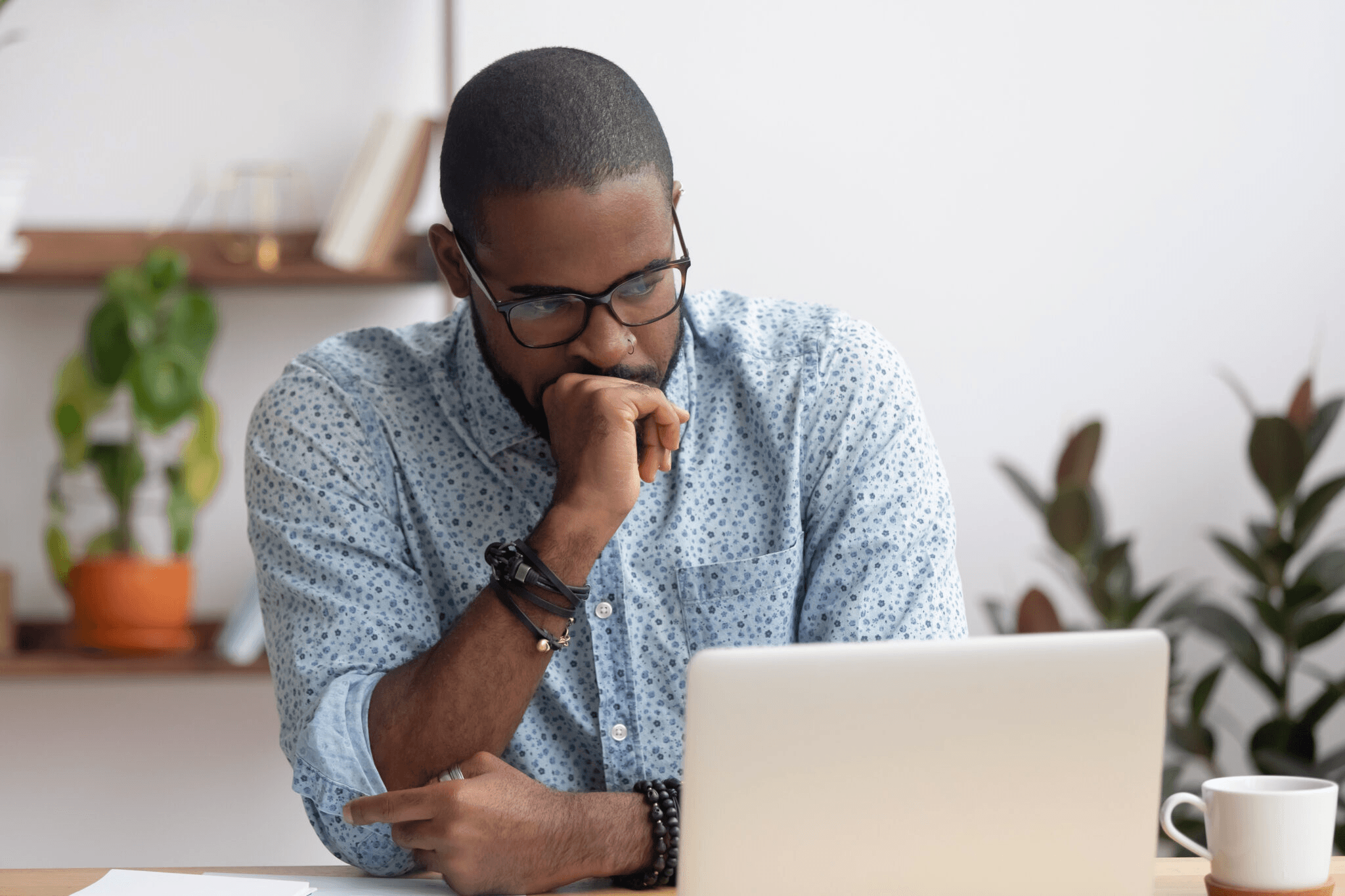 African American man with glasses in a blue shirt staring contemplatively at a laptop