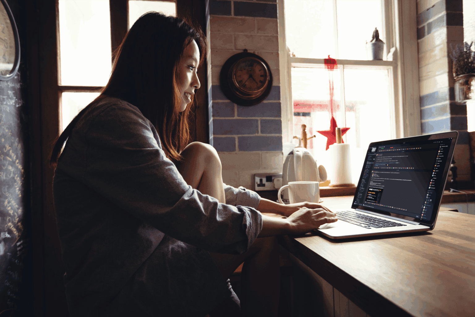 Person working on a laptop at a kitchen table in a softly lit home setting