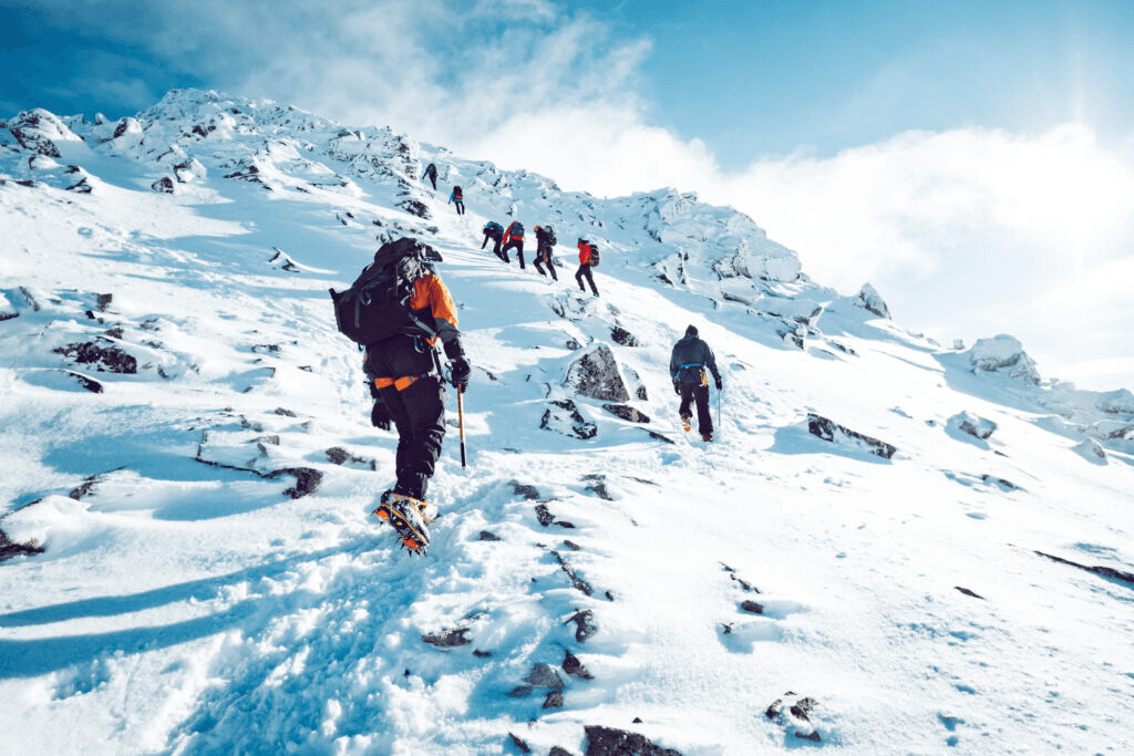 A group of climbers hiking up a snowy mountain ridge with backpacks and ice axes.