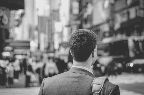 Black-and-white rear view of a man with a shoulder bag overlooking a busy city street.